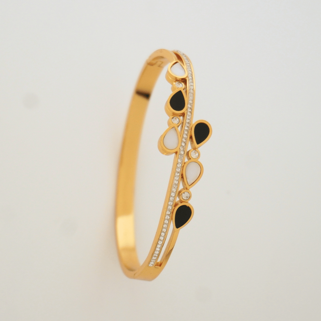 Gold bracelet with black and white stones on a light gray background